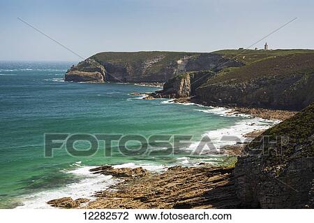 Stock Image - Rocky shoreline and bay with tower in the background and blue sky; Frehel, Brittany, France. Fotosearch