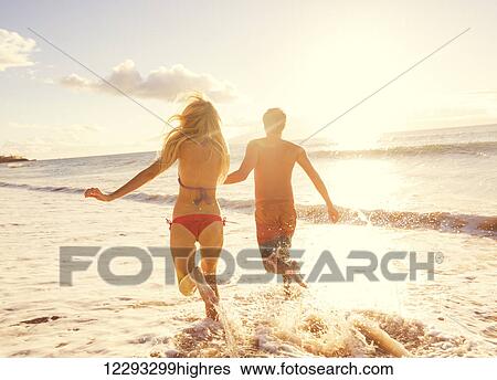 Stock Photograph - Romantic Couple Enjoying Sunset on Beautiful Tropical Beach. Fotosearch