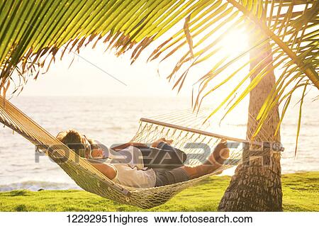 Romantic couple relaxing in tropical hammock at sunset View Large Photo Image Stock Photograph - Romantic couple relaxing in tropical hammock at sunset. Fotosearch