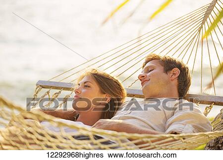 Romantic couple relaxing in tropical hammock at sunset View Large Photo Image Stock Photograph - Romantic couple relaxing in tropical hammock at sunset. Fotosearch