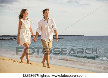 Romantic happy couple walking on beach at sunset. Smiling with arms around each other. Man and woman in love View Large Photo Image Stock Photograph - Romantic happy couple walking on beach at sunset. Smiling with arms around each other. Man and woman in love. Fotosearch