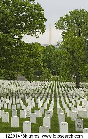 Stock Photograph - Rows of grave stones at Arlington National Cemetery, with the Washington Monument across the river in Washington, D. C.; Arlington, Virginia, United States of America. Fotosearch