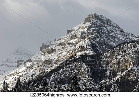 Stock Photograph - Rugged mountain peak with snow under a cloudy sky; Lake Louise, Alberta, Canada. Fotosearch