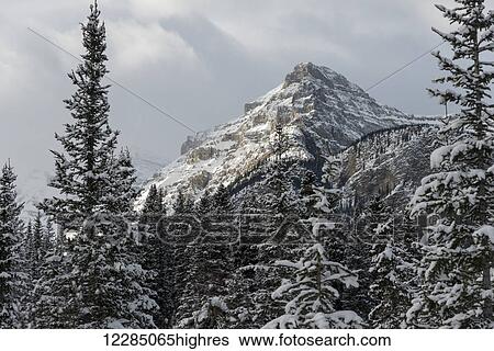 Stock Photograph - Rugged mountain peak with snow under a cloudy sky; Lake Louise, Alberta, Canada. Fotosearch