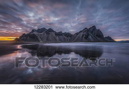 Rugged mountain peaks and a colourful sunset reflected in tranquil water; Iceland View Large Photo Image Stock Image - Rugged mountain peaks and a colourful sunset reflected in tranquil water; Iceland. Fotosearch