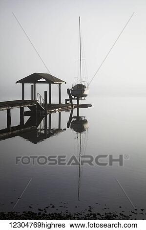 Stock Photograph - Sailboat on lift by dock on foggy lake; Bellingham, Washington, United States of America. Fotosearch