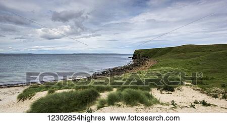 Stock Photograph - Sand and grass on the shore with a view of the coastline; Caithness, Scotland. Fotosearch