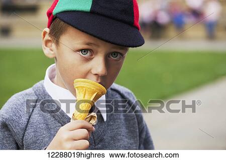 Stock Photograph - Serious schoolboy in a uniform eating an ice cream cone; London, England. Fotosearch