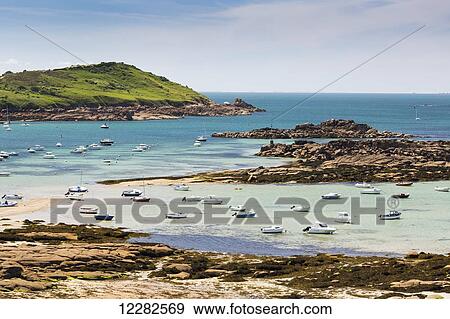 Stock Photo - Several boats in a rocky cove at low tide with a grassy hillside in the background; Trebeurden, Brittany, France. Fotosearch