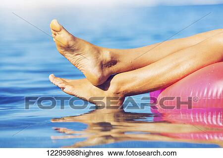 Stock Photograph - Sexy young woman in bikini relaxing floating in the ocean, close up view of legs and feet. Fotosearch
