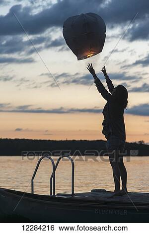 Silhouette of a girl releasing a lit paper lantern into the air at sunset; Lake of the Woods, Ontario, Canada View Large Photo Image Stock Photograph - Silhouette of a girl releasing a lit paper lantern into the air at sunset; Lake of the Woods, Ontario, Canada. Fotosearch