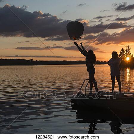 Silhouette of a teenage girl releasing a lit lantern out over a lake at sunset; Lake of the Woods, Ontario, Canada View Large Photo Image Stock Image - Silhouette of a teenage girl releasing a lit lantern out over a lake at sunset; Lake of the Woods, Ontario, Canada. Fotosearch