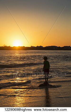 Silhouette of a young boy standing at the water's edge at sunset; Caloundra, Queensland, Australia View Large Photo Image Stock Photograph - Silhouette of a young boy standing at the water's edge at sunset; Caloundra, Queensland, Australia. Fotosearch