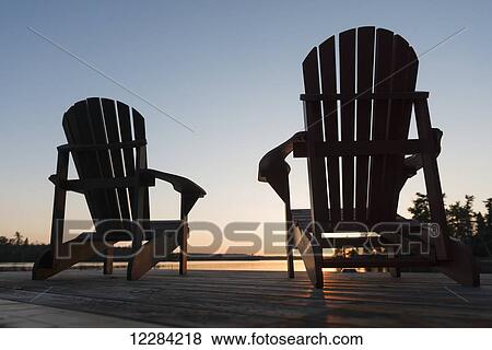 Stock Photo - Silhouette of adirondack chairs on a wooden dock along a lake at sunset; Ontario, Canada. Fotosearch