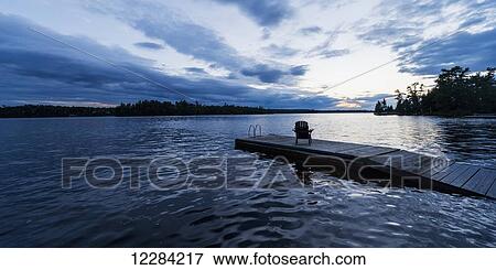 Silhouette of an adirondack chair on a wooden dock along a lake at sunset; Ontario, Canada View Large Photo Image Stock Photo - Silhouette of an adirondack chair on a wooden dock along a lake at sunset; Ontario, Canada. Fotosearch