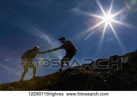 Silhouette of male hiker helping female hiker up a rocky slope with blue sky and sun burst; Waterton, Alberta, Canada View Large Photo Image Stock Photograph - Silhouette of male hiker helping female hiker up a rocky slope with blue sky and sun burst; Waterton, Alberta, Canada. Fotosearch