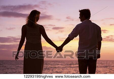 Stock Photograph - Silhouette of Romantic couple watching tropical sunset on the beach. Fotosearch