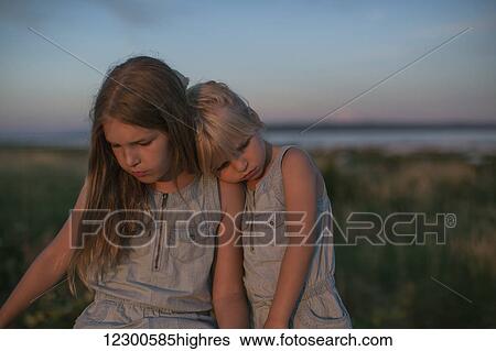 Stock Photograph - Sisters sitting together on the beach at sunset; Surrey, British Columbia, Canada. Fotosearch