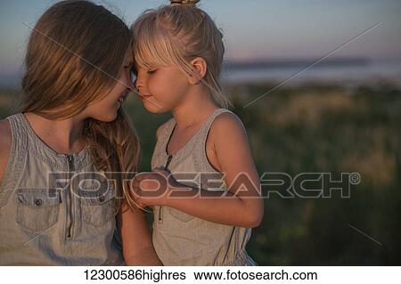 Stock Photograph - Sisters sitting together on the beach at sunset; Surrey, British Columbia, Canada. Fotosearch