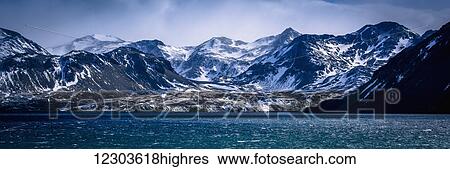 Stock Photograph - Snowy mountains in sunshine beside blue sea; Antarctica. Fotosearch