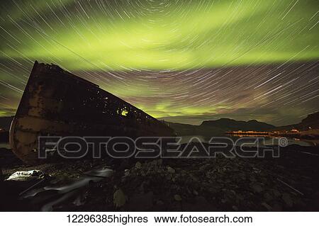Stock Photograph - Star trails and northern lights over top the town of Djupavik in the West Fjords of Iceland; Djupavik, Iceland. Fotosearch