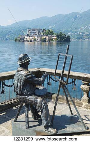 Stock Photo - Statue of an artist sitting and painting at an easel with a view of San Giulio Island on Lake Orta; Orta, Piedmont, Italy. Fotosearch