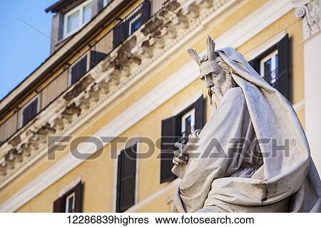 Stock Photograph - Statue of historical male figure and yellow building; Rome, Italy. Fotosearch