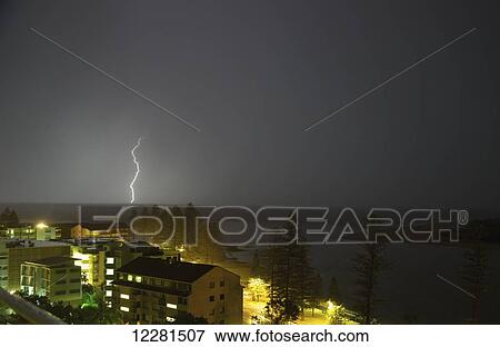 Stock Photo - Storm clouds and lightening striking over a city; Caloundra, Queensland, Australia. Fotosearch
