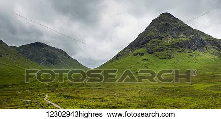 Stock Photograph - Storm clouds over rugged and foliage covered mountains; Scotland. Fotosearch