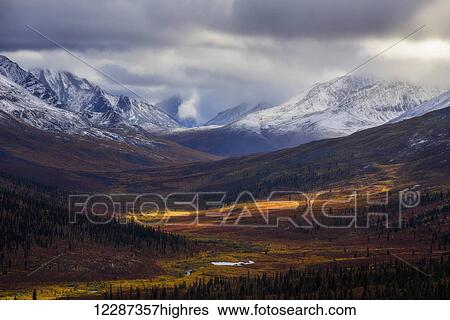 Stock Photograph - Storm clouds part allowing light to illuminate the landcape in the North Klondike Valley along the Dempster Highway in northern Yukon; Yukon, Canada. Fotosearch