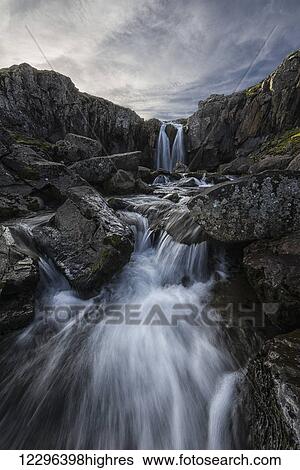 Stock Photograph - Stream flows over a waterfall along the eastern coast of Iceland; Iceland. Fotosearch