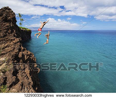 Stock Photograph - Summer fun, Friends cliff jumping into the ocean.. Fotosearch