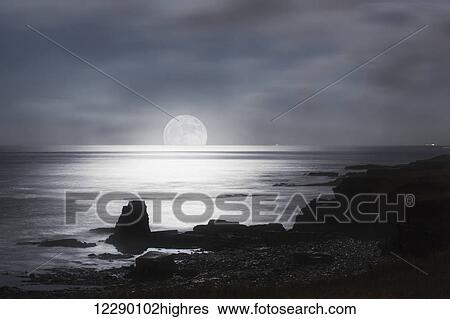 Stock Photograph - Sun rising over the horizon of the ocean with a silhouetted coastline; South Shields, Tyne and Wear, England. Fotosearch