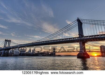 Stock Photograph - Sun setting behind Manhattan and Brooklyn Bridges; New York City, New York, United States of America. Fotosearch