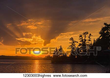 Sunrise casting an orange glow over the sky and reflected in a tranquil lake; Ontario, Canada View Large Photo Image Stock Photograph - Sunrise casting an orange glow over the sky and reflected in a tranquil lake; Ontario, Canada. Fotosearch