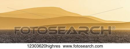 Stock Photograph - Sunrise over orange hills and blue ocean; Antarctica. Fotosearch