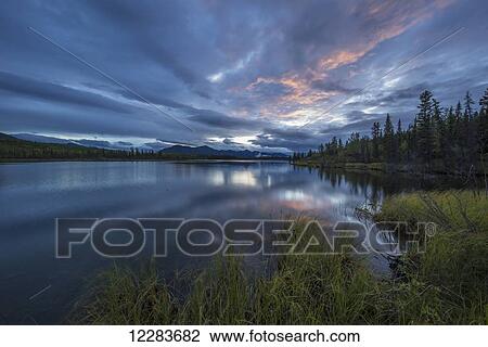 Stock Image - Sunset lights up a swath of clouds over Jackfish Lake; Yukon, Canada. Fotosearch