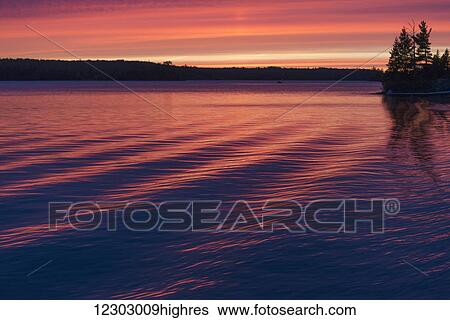 Stock Photograph - Sunset over a lake reflecting pink on the tranquil water; Ontario, Canada. Fotosearch