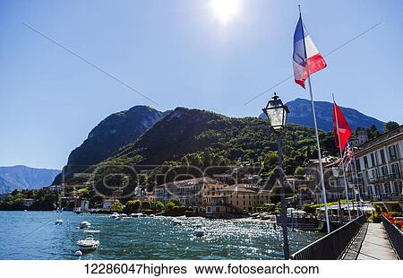 Stock Photograph - Sunshine on the Italian flag and waterfront views from the town of Menaggio on Lake Como; Menaggio, Lombardy, Italy. Fotosearch