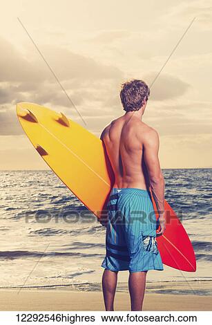 Stock Photograph - Surfer on the beach at sunset in Hawaii. Fotosearch