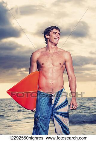 Stock Photograph - Surfer on the beach at sunset in Hawaii. Fotosearch
