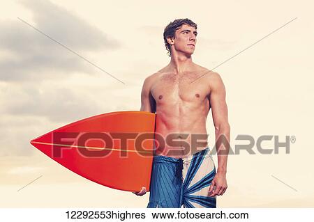 Stock Photograph - Surfer on the beach at sunset in Hawaii. Fotosearch