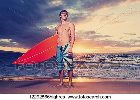 Stock Photograph - Surfer on the beach at sunset in Hawaii. Fotosearch