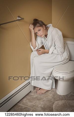 Stock Photograph - Teenage girl sitting in the bathroom on the toilet seat looking unhappy. Fotosearch