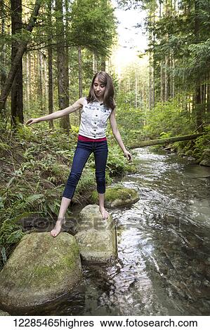 Stock Photograph - Teenage girl walking barefoot over rocks in a stream; Chilliwack, British Columbia, Canada. Fotosearch