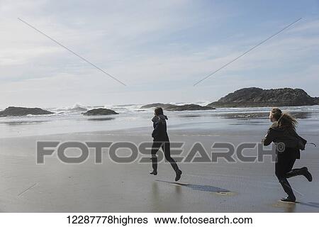 Stock Photograph - Teenage girls running on a wet beach at the coast, Vancouver Island; Tofino, British Columbia, Canada. Fotosearch