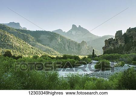 Stock Photograph - The early morning sun illuminates a green river valley and sharp mountain peaks; Argentina. Fotosearch