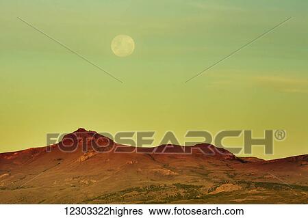 Stock Photograph - The moon is rising over a yellow desert landscape; Bariloche, Argentina. Fotosearch