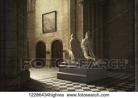 Stock Photograph - The statue of a royal couple caught in beautiful light in the grandiose Basilica of Saint Denis; Paris, France. Fotosearch