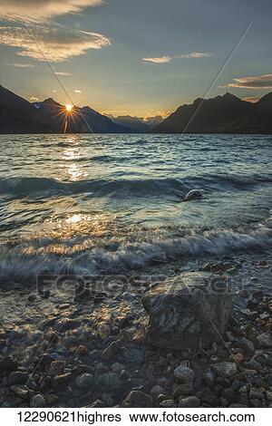 Stock Photograph - The sun rises as soft waves brush the shoreline of upper Twin Lake in Lake Clark National Park & Preserve, Alaska.. Fotosearch